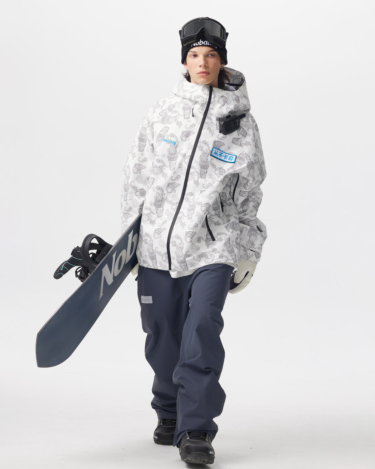 Model wearing the white paisley-print Nobaday Dawn Print 3L Zip-Up Snow Jacket while carrying a snowboard