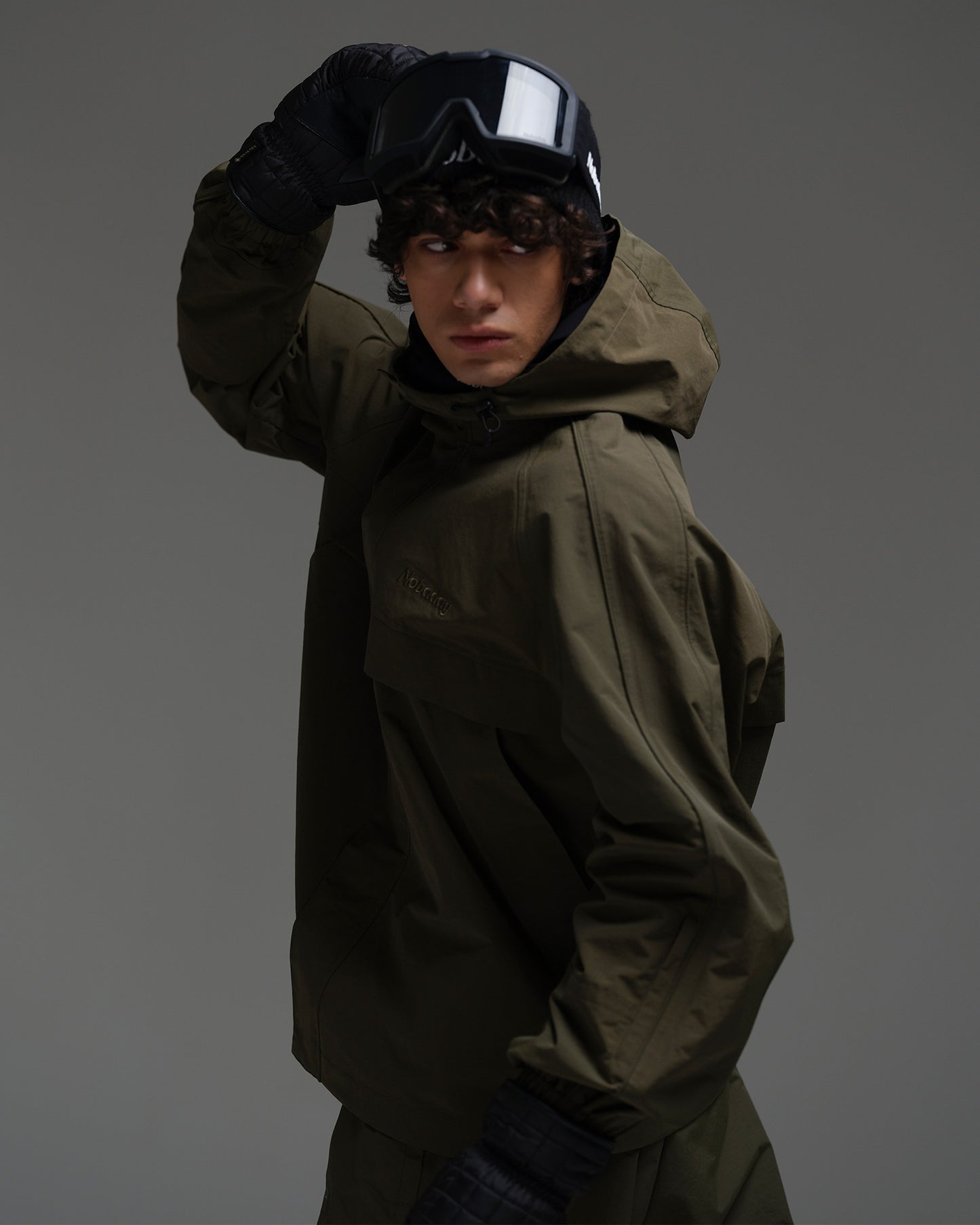 Side view of a man wearing a dark green NOBADAY Pure Free snow jacket with an adjustable hood