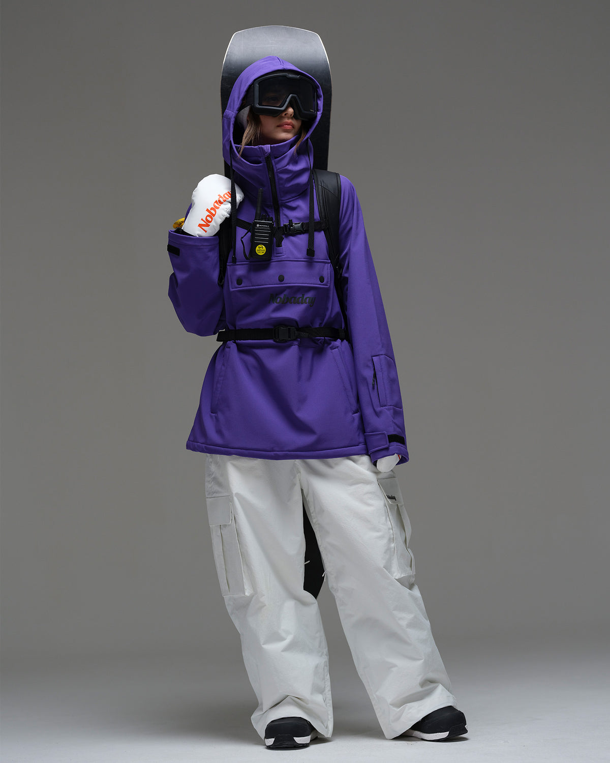 Full body view of Nobaday Women's Pure Free purple waterproof fleece hoodie with white snow pants and snowboard gear