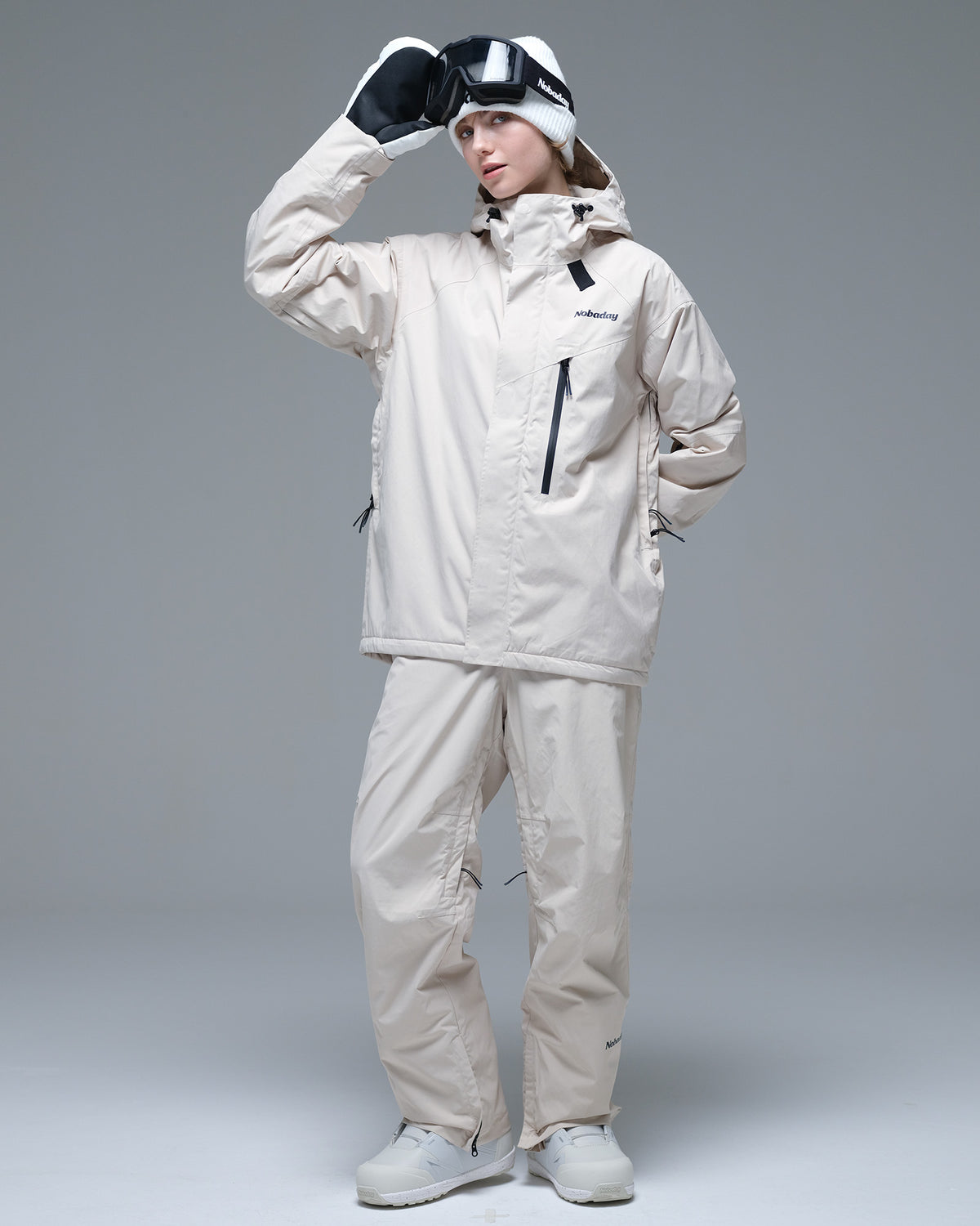 Full-body view of a woman wearing the NOBADAY Women's Baggy Insulated beige snow jacket with matching snow pants