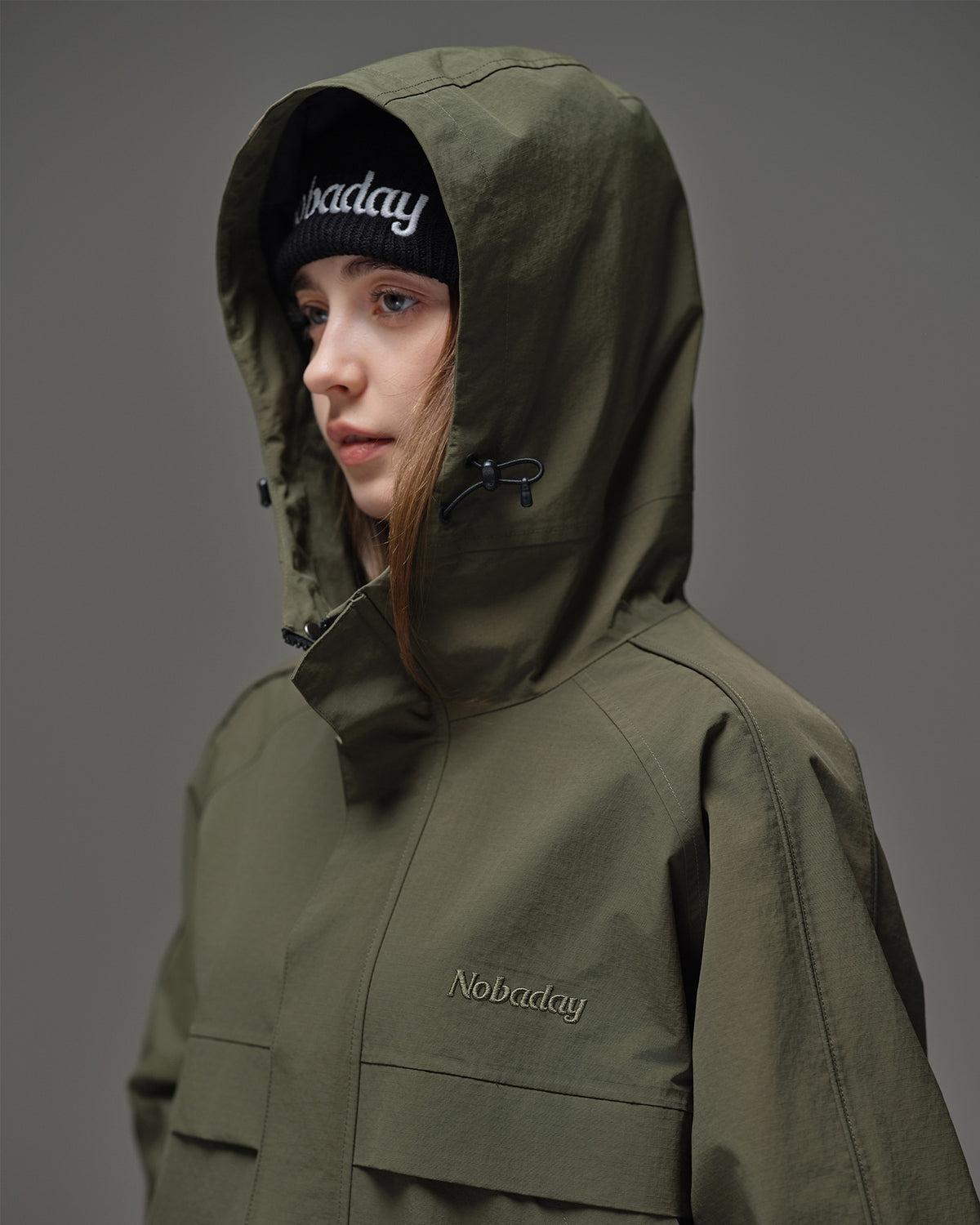 Close-up of Nobaday women's green cargo snow jacket showing oversized adjustable hood, high collar, and embroidered logo detail