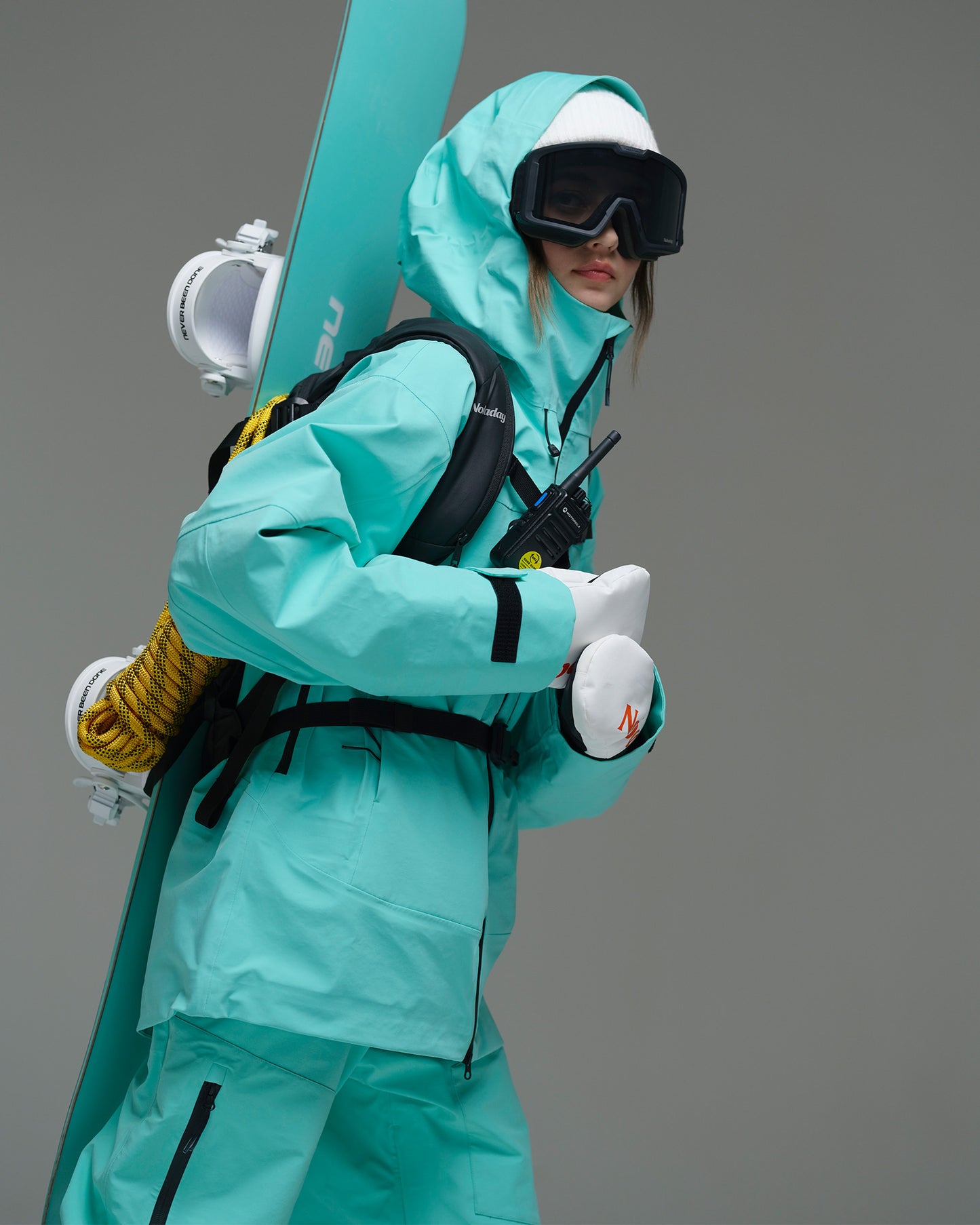 Woman wearing the Nobaday Pure Free Apex 3L waterproof breathable snow jacket in blue with a snowboard backpack and communication radio