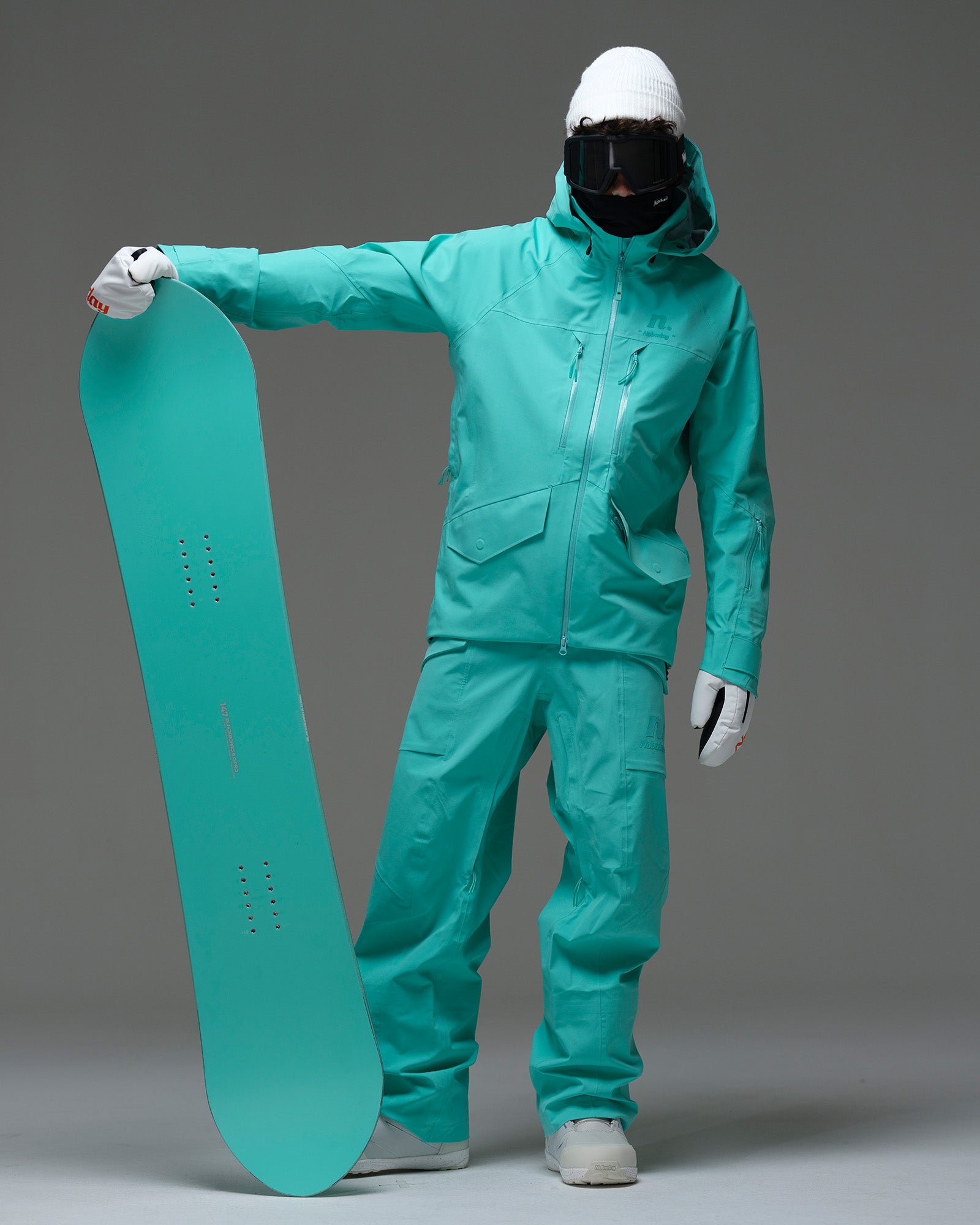 Full-body view of a male snowboarder wearing the NOBADAY Men’s ArcticStorm Freeride 3L blue snow jacket and matching snow pants while holding a snowboard