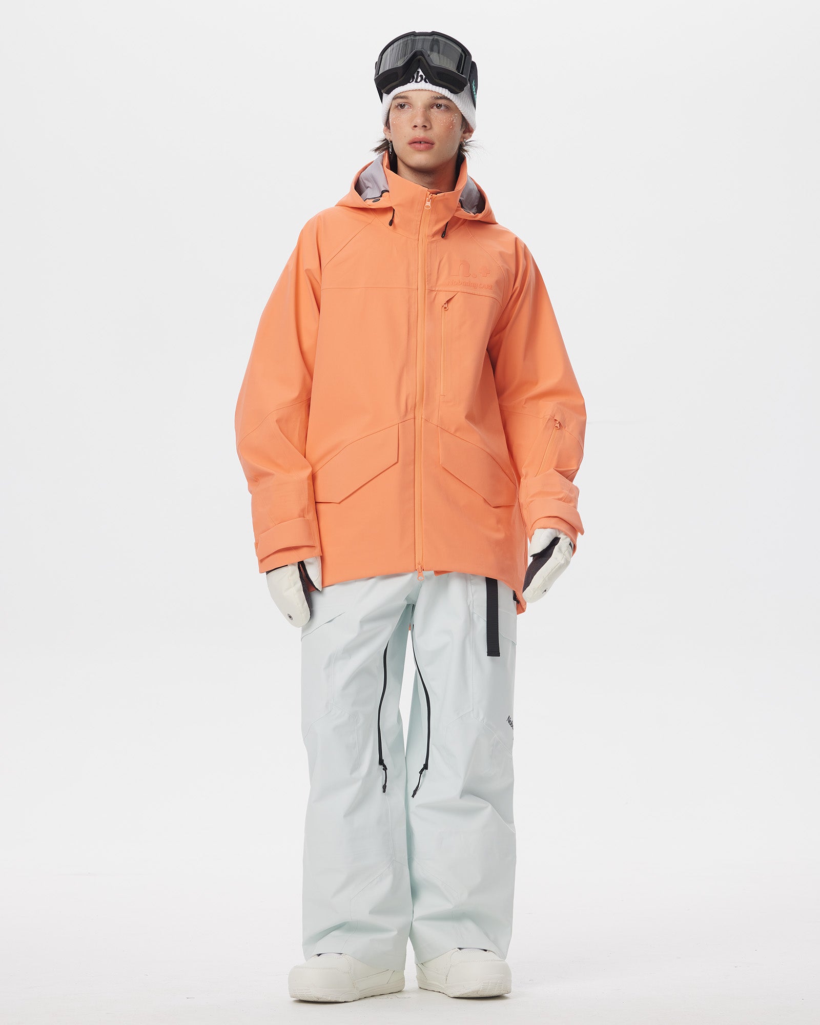 Full-body front view of a male model wearing the Nobaday ArcticStorm Freeride Orange 3L Snow Jacket with white snow pants