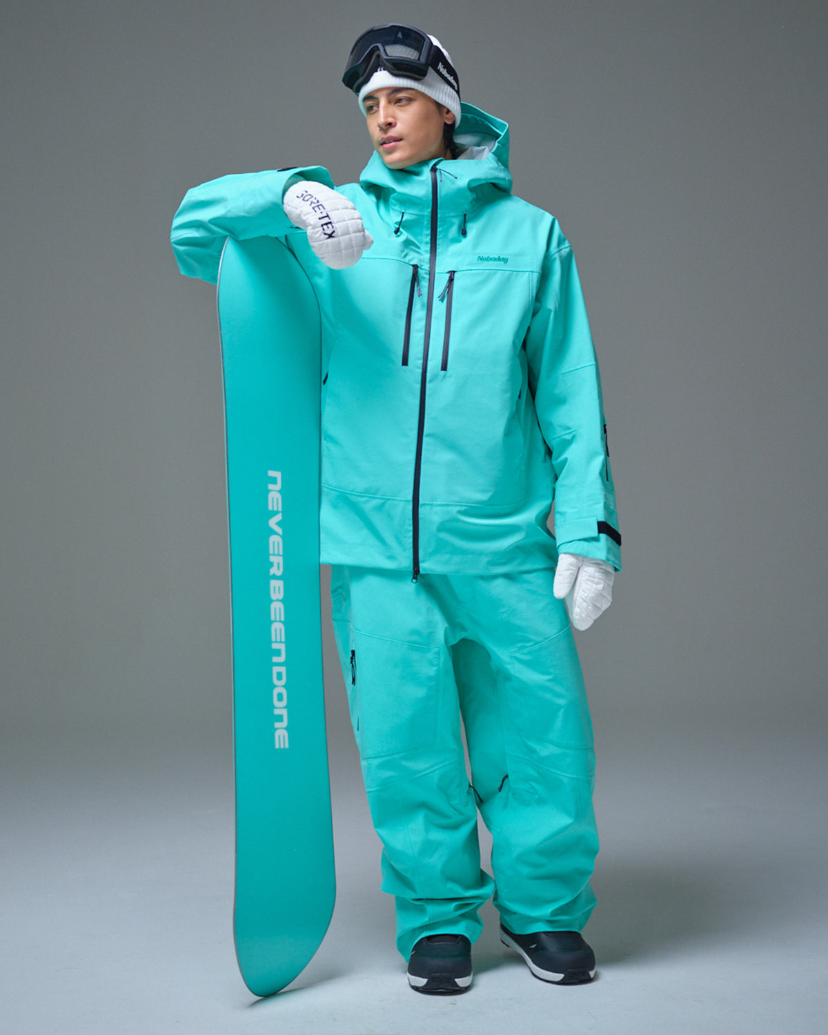 Man wearing the Nobaday Blue Apex 3L snow jacket and matching pants while holding a snowboard