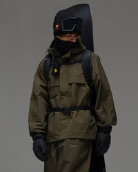 Man wearing a dark green NOBADAY snow jacket with a snowboard, backpack and winter gear