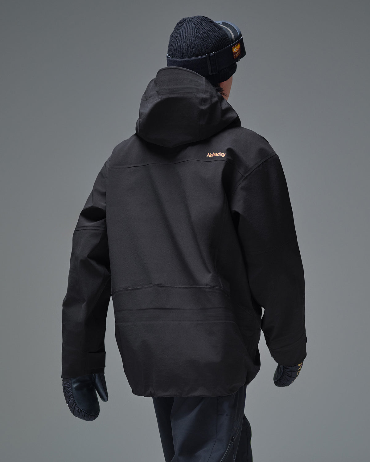 Back view of the black NOBADAY Pure Free Apex 3L snow jacket with a hood and orange logo
