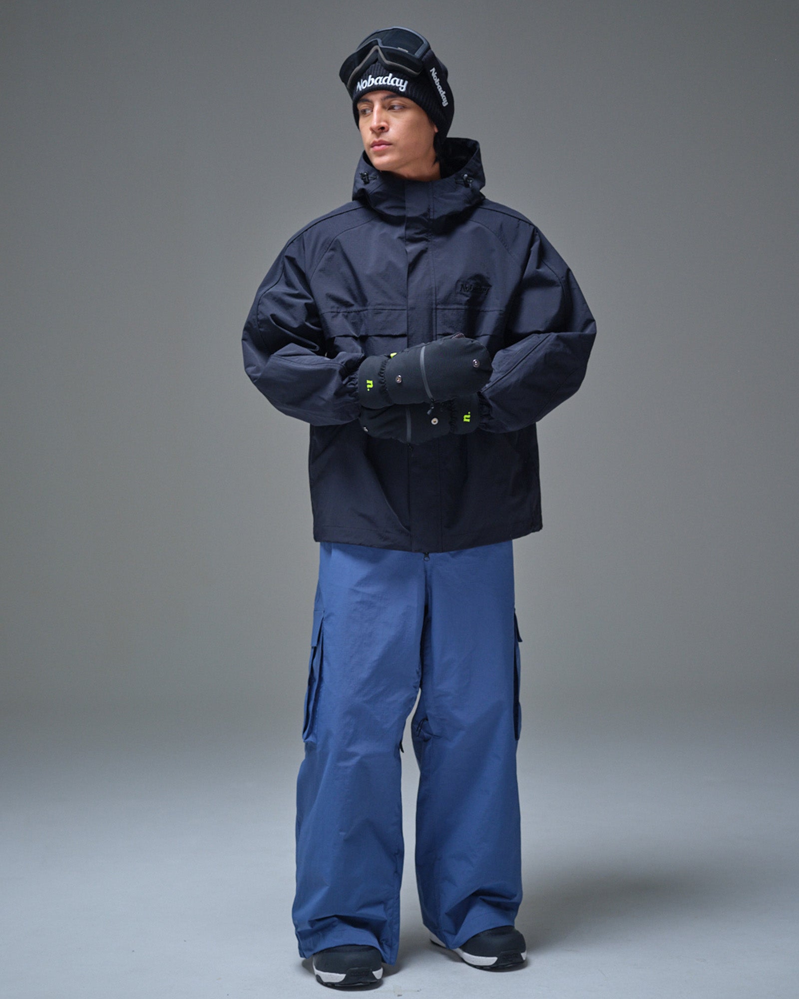 Full-body view of a man wearing the black NOBADAY Pure Free snow jacket and blue snow pants