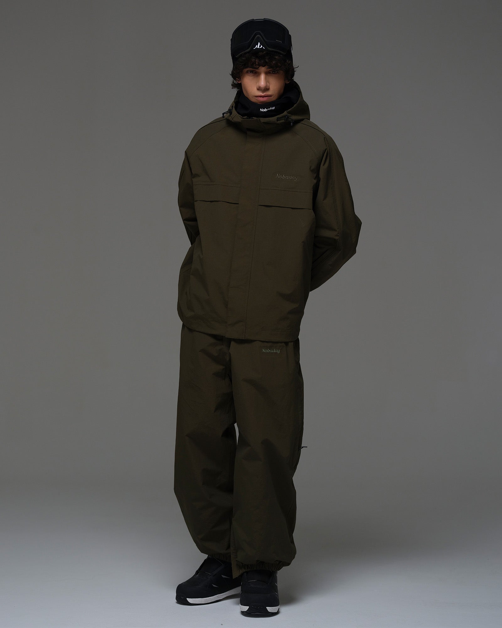 Full-body view of a man wearing a dark green NOBADAY Pure Free snow jacket and matching snow pants