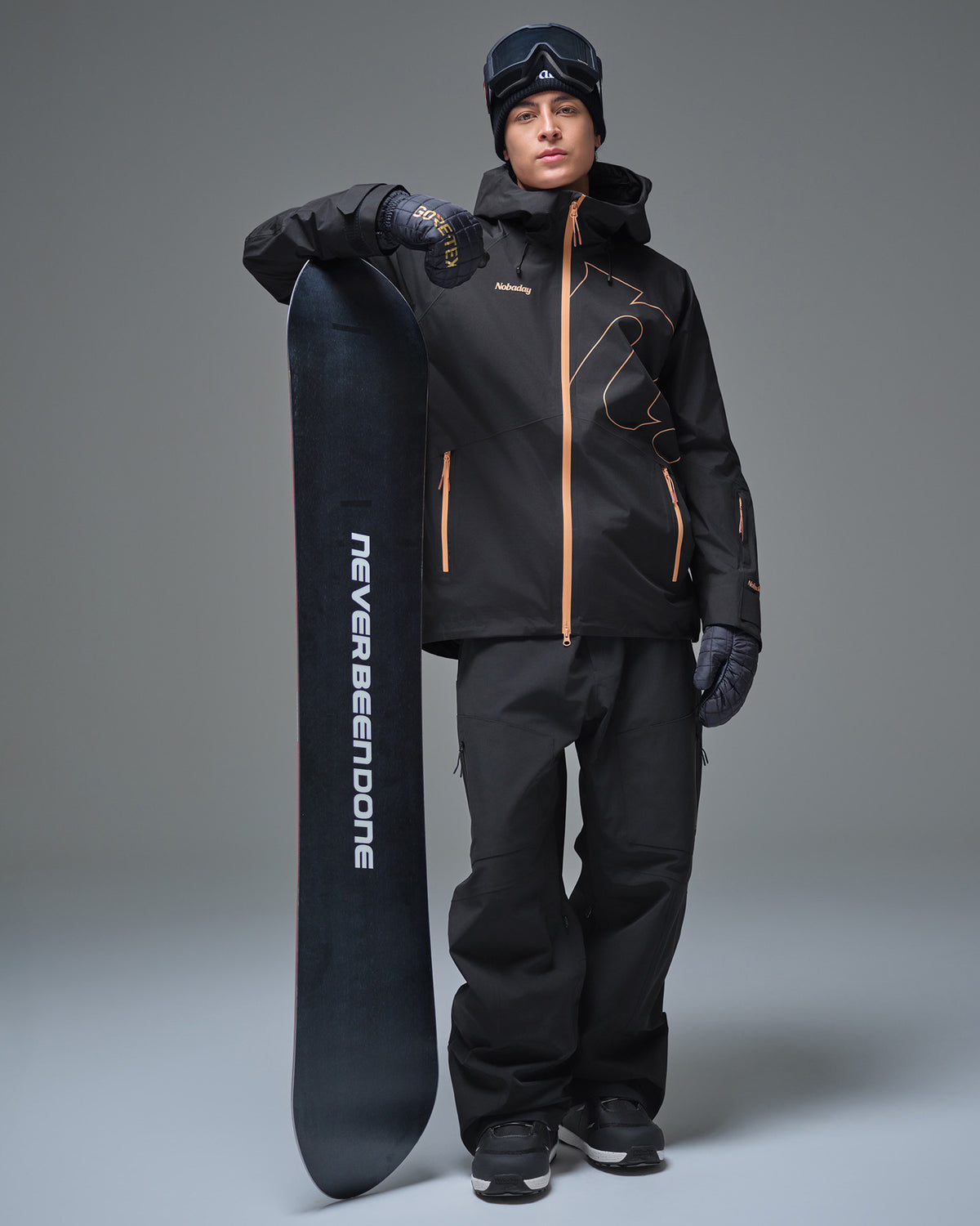 Full-body view of a man wearing the Black NOBADAY Men’s Summit GORE-TEX snow jacket while holding a snowboard