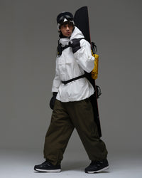 Man wearing a white NOBADAY snow jacket while carrying a snowboard and backcountry gear