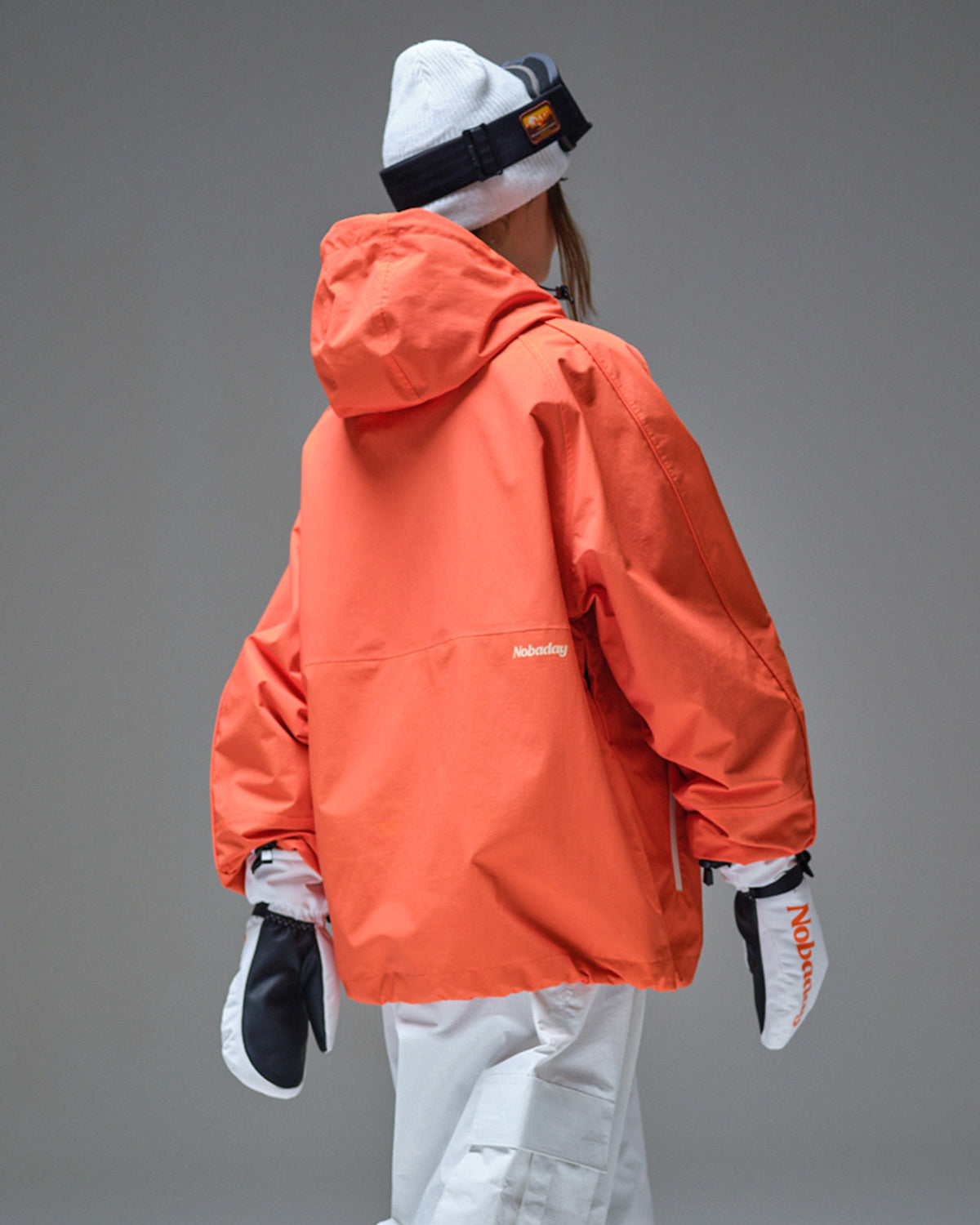Back view of Nobaday orange active snow jacket showing oversized hood, relaxed fit, waterproof shell, and white snow pants
