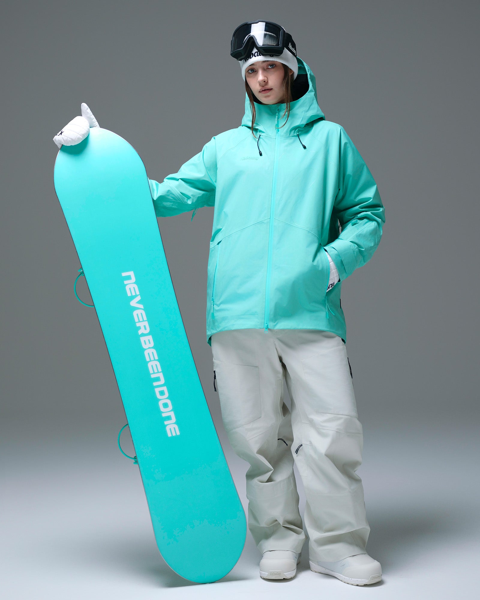 Full-body view of a woman wearing a Nobaday Blue GORE-TEX snow jacket while holding a snowboard
