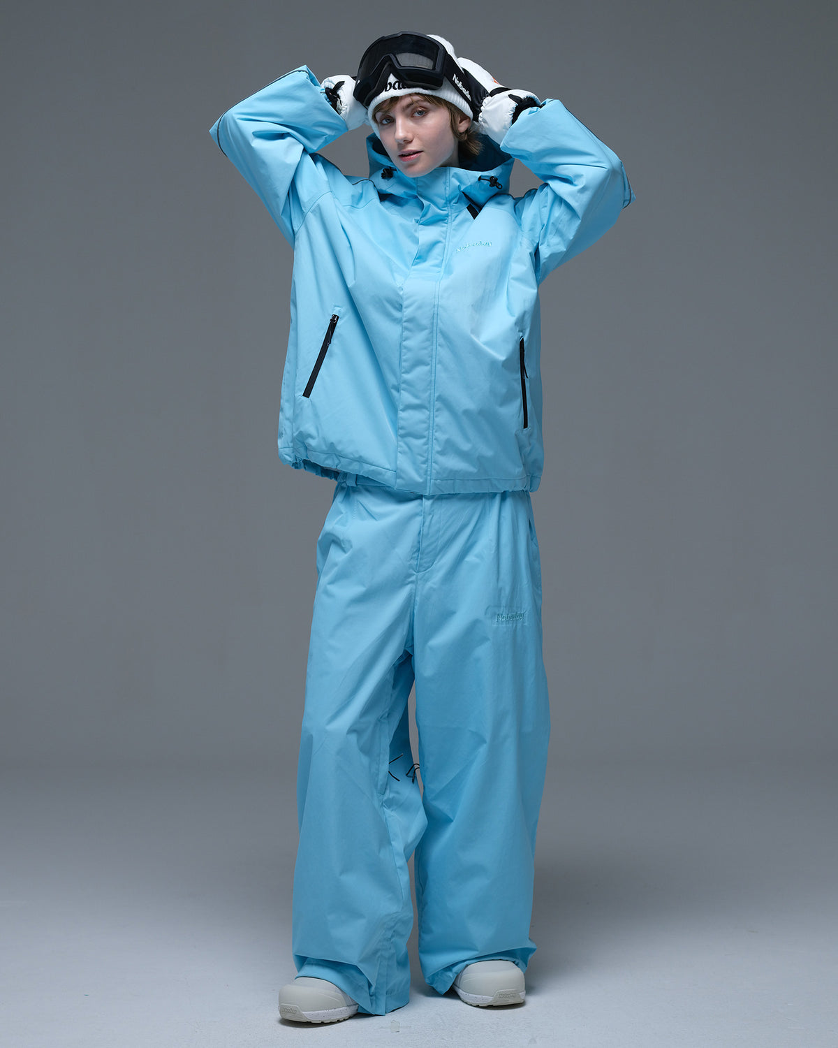 Full-body action pose of a woman wearing the NOBADAY Women's Dawn OG Insulated ice blue snow jacket with matching snow pants