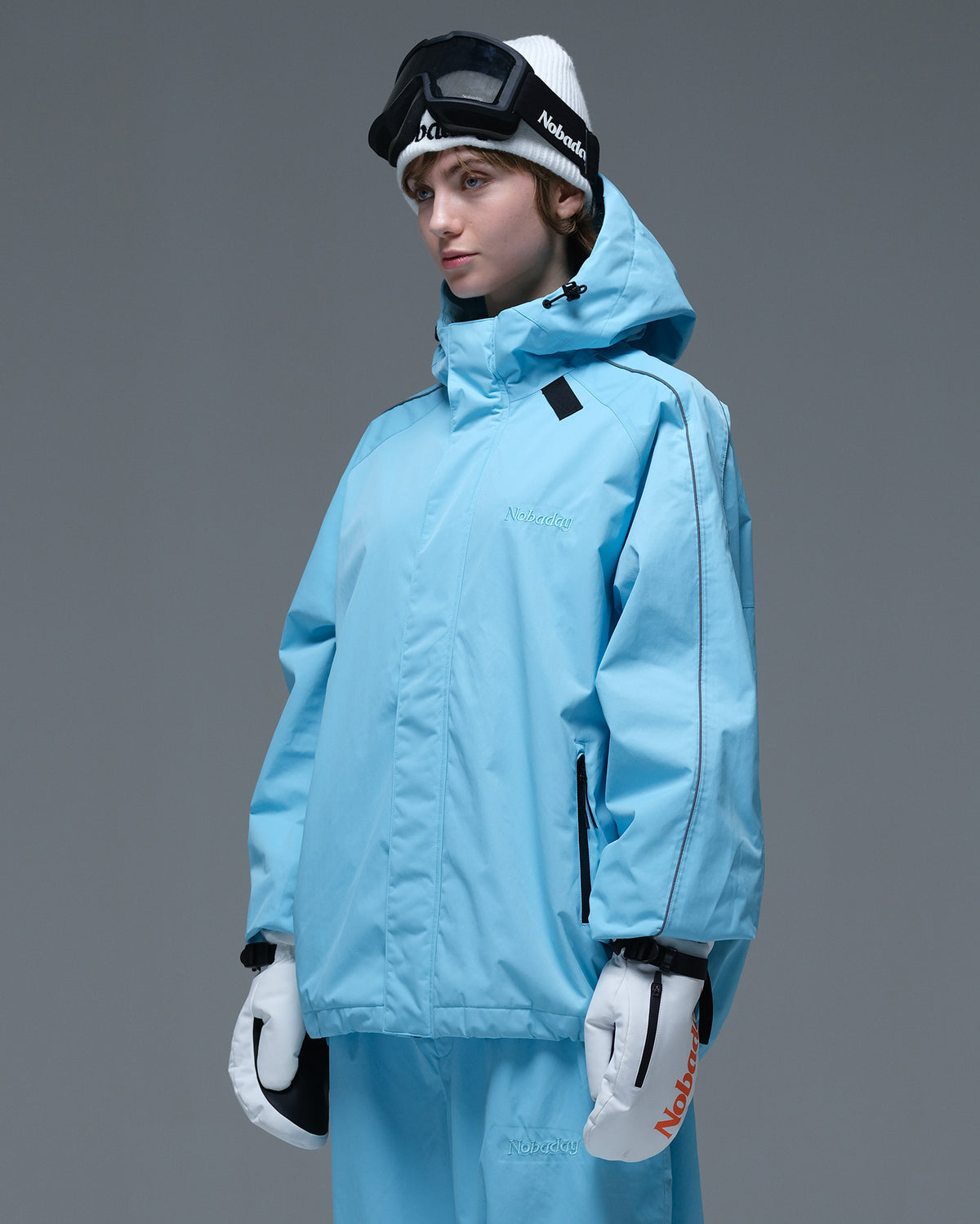 Side view of the NOBADAY Women's Dawn OG Insulated ice blue snow jacket showing its oversized fit, storm hood, and zippered pocket