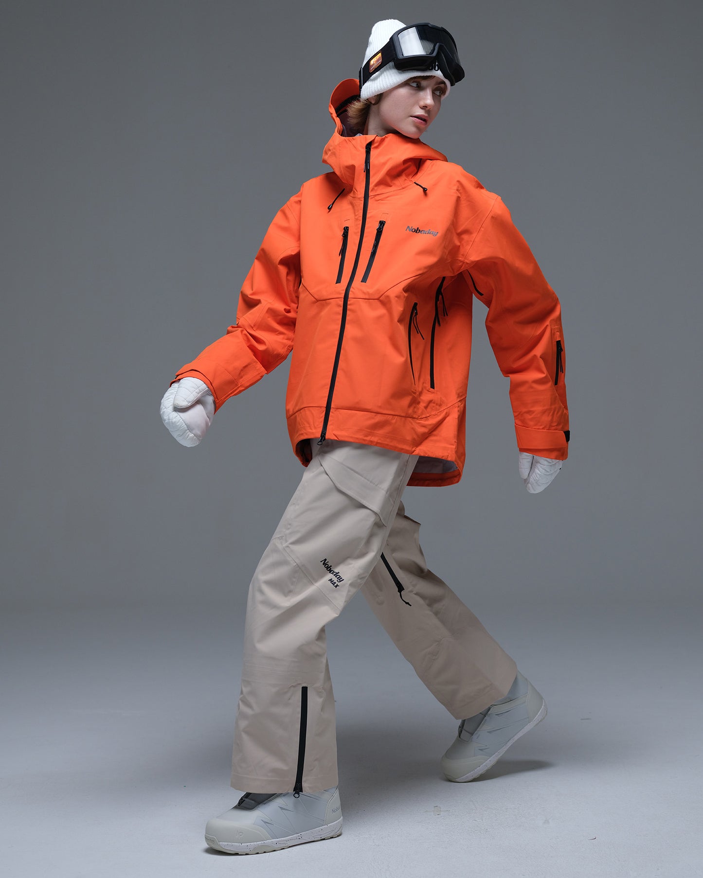 Full-body action view of a model wearing the orange Nobaday Women’s MaxExtreme Pro Zip-Up 3L Snow Jacket with beige snow pants