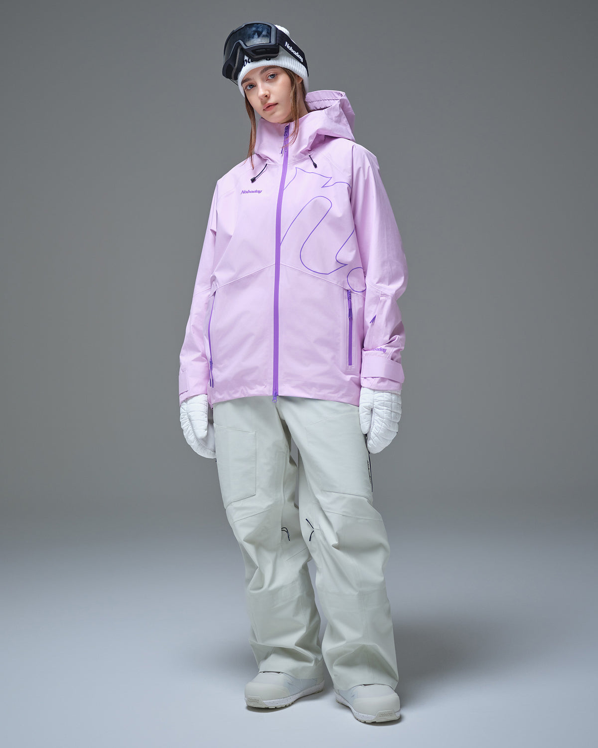 Full-body view of a woman wearing a pink NOBADAY GORE-TEX snow jacket and white snow pants