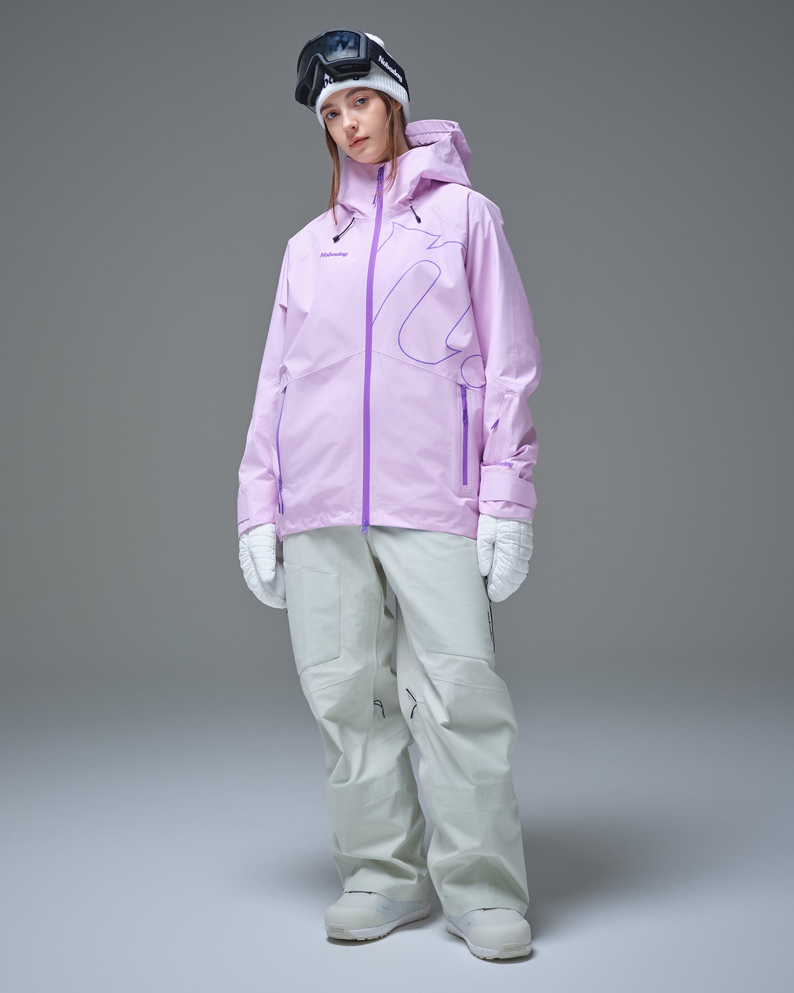 Full-body view of a woman wearing a pink NOBADAY GORE-TEX snow jacket and white snow pants