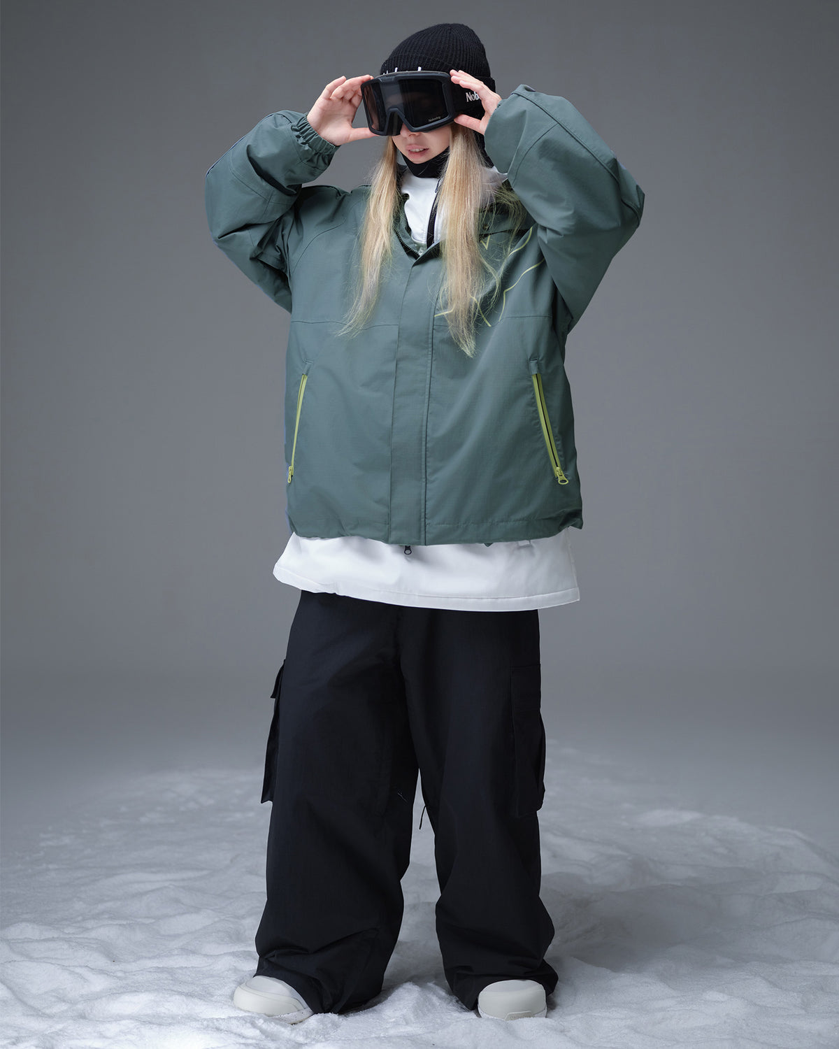 Nobaday Women's Pure Free Active green snow jacket layered over a white midlayer with goggles, oversized sleeves, and snowboard fit
