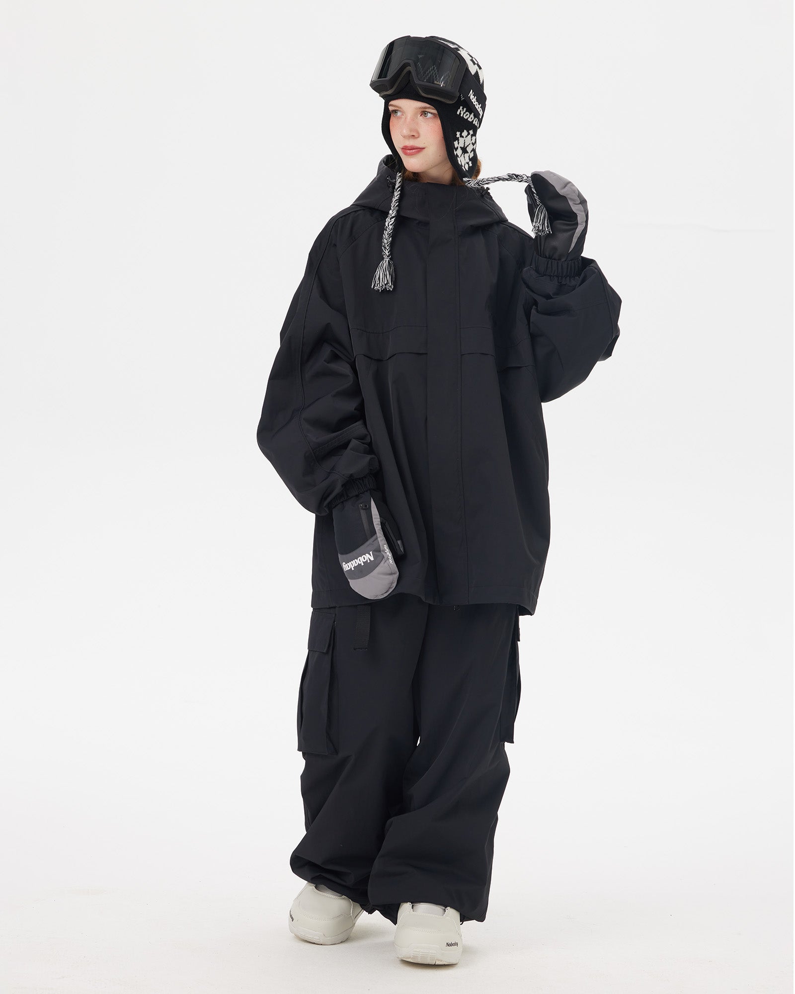 Full body view of Nobaday Women's Pure Free black snow jacket with oversized fit, protective hood, snow goggles, and black snow pants