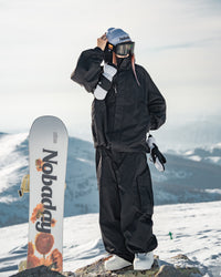 Nobaday Women's Pure Free black snow jacket worn outdoors on snowy mountain with snowboard, goggles, mittens, and black snow pants
