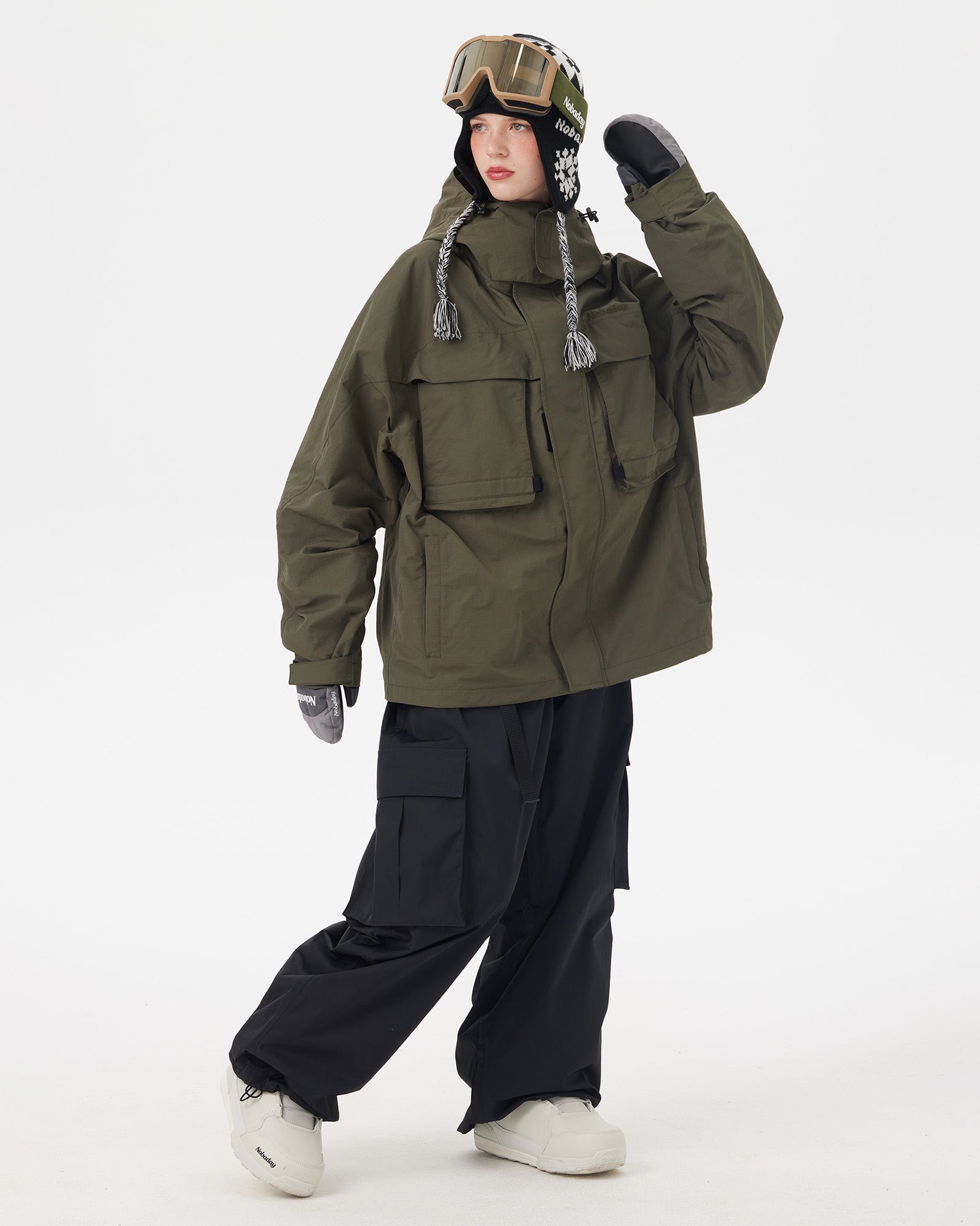 Full-body action pose of a woman wearing the NOBADAY Women's Pure Free Freestyle dark green snow jacket with black cargo snow pants