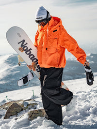 Female snowboarder wearing the NOBADAY Women's Pure Free Freestyle orange waterproof snow jacket while carrying a snowboard on a snowy mountain